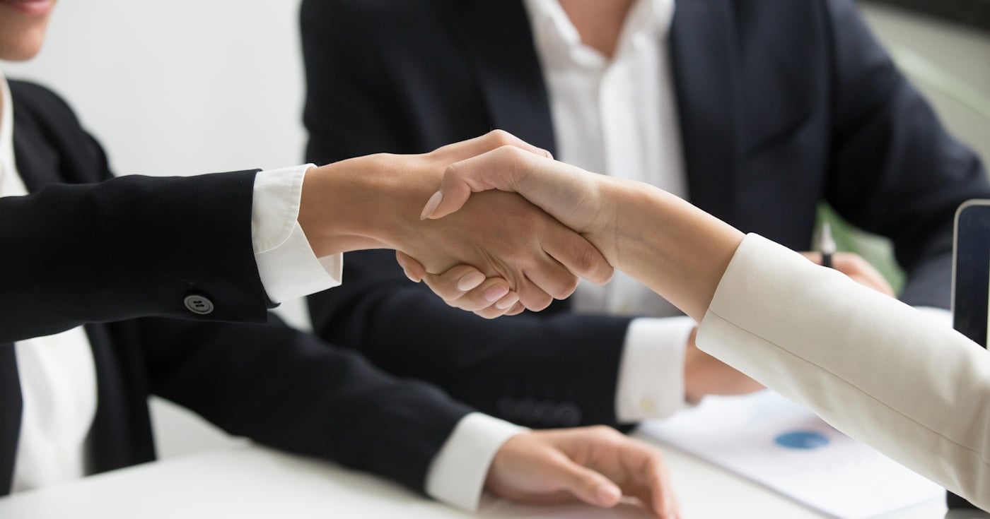 Two professionals shaking hands in front of a laptop — advisory shares agreement