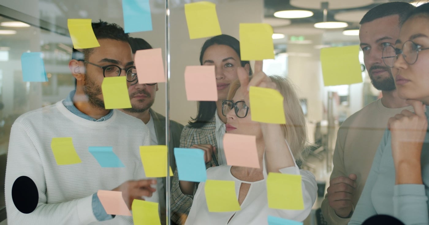 Diverse team working with sticky notes on a whiteboard, brainstorming business model canvas