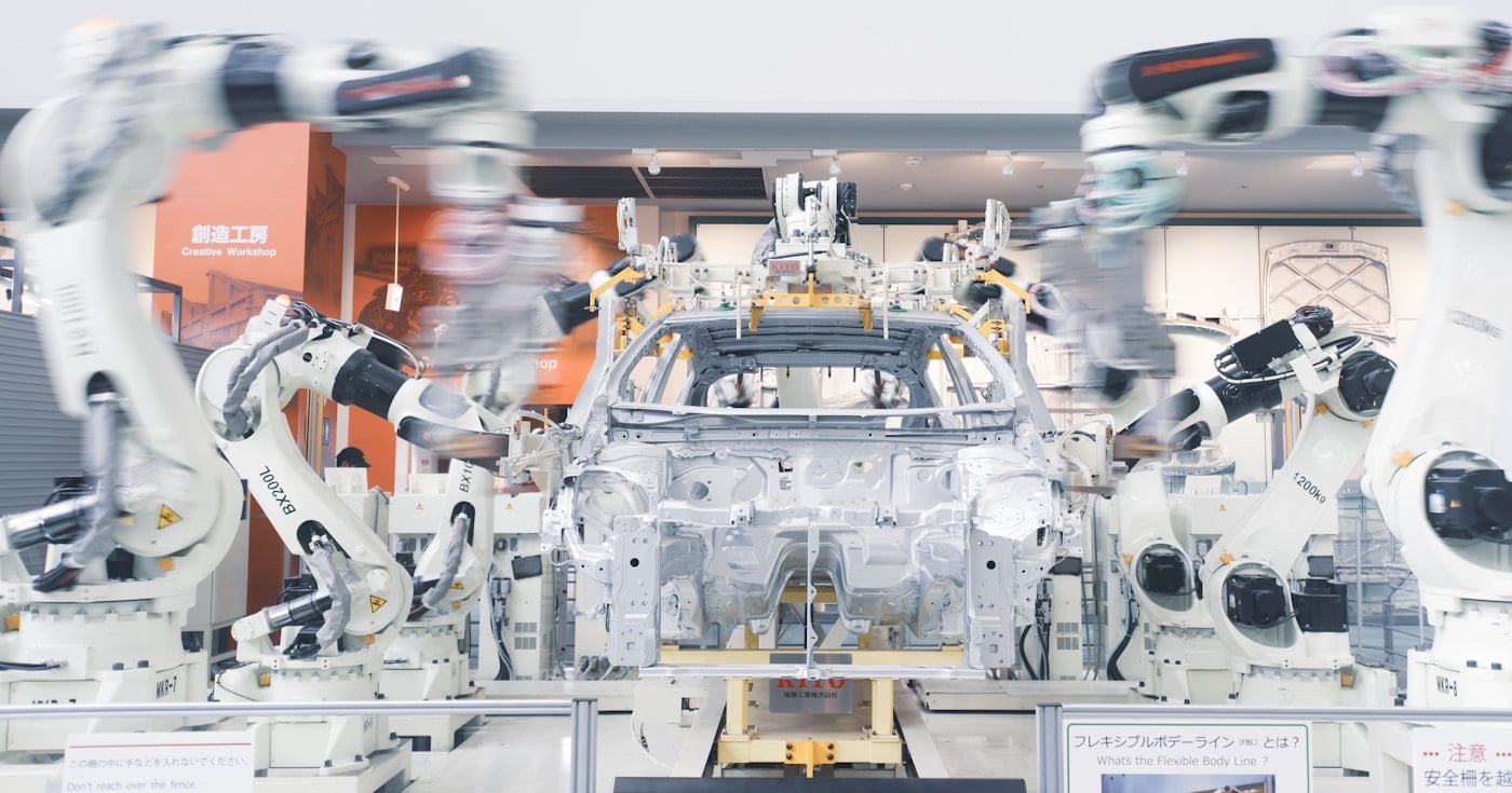 Robotic arms assembling a car chassis on a factory line, illustrating the Elon Musk Algorithm applied to manufacturing