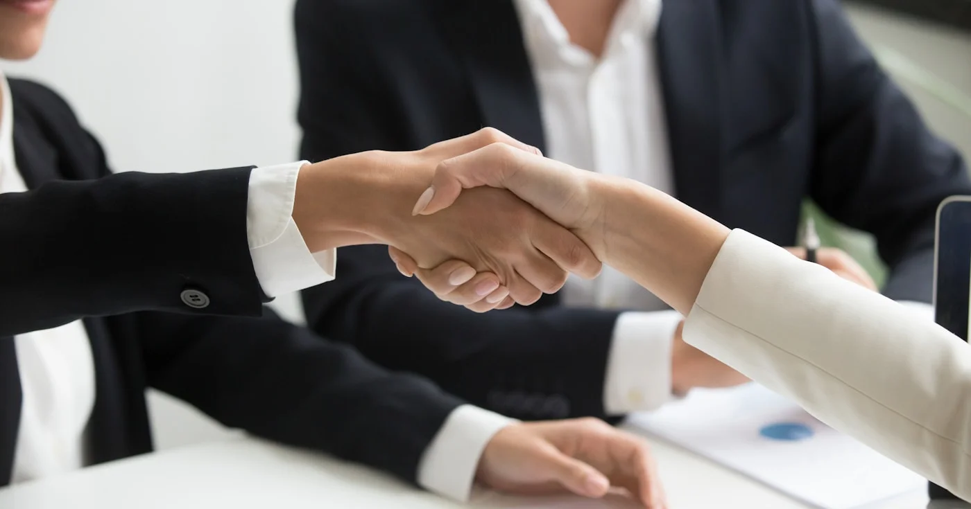 Two professionals shaking hands in front of a laptop — advisory shares agreement