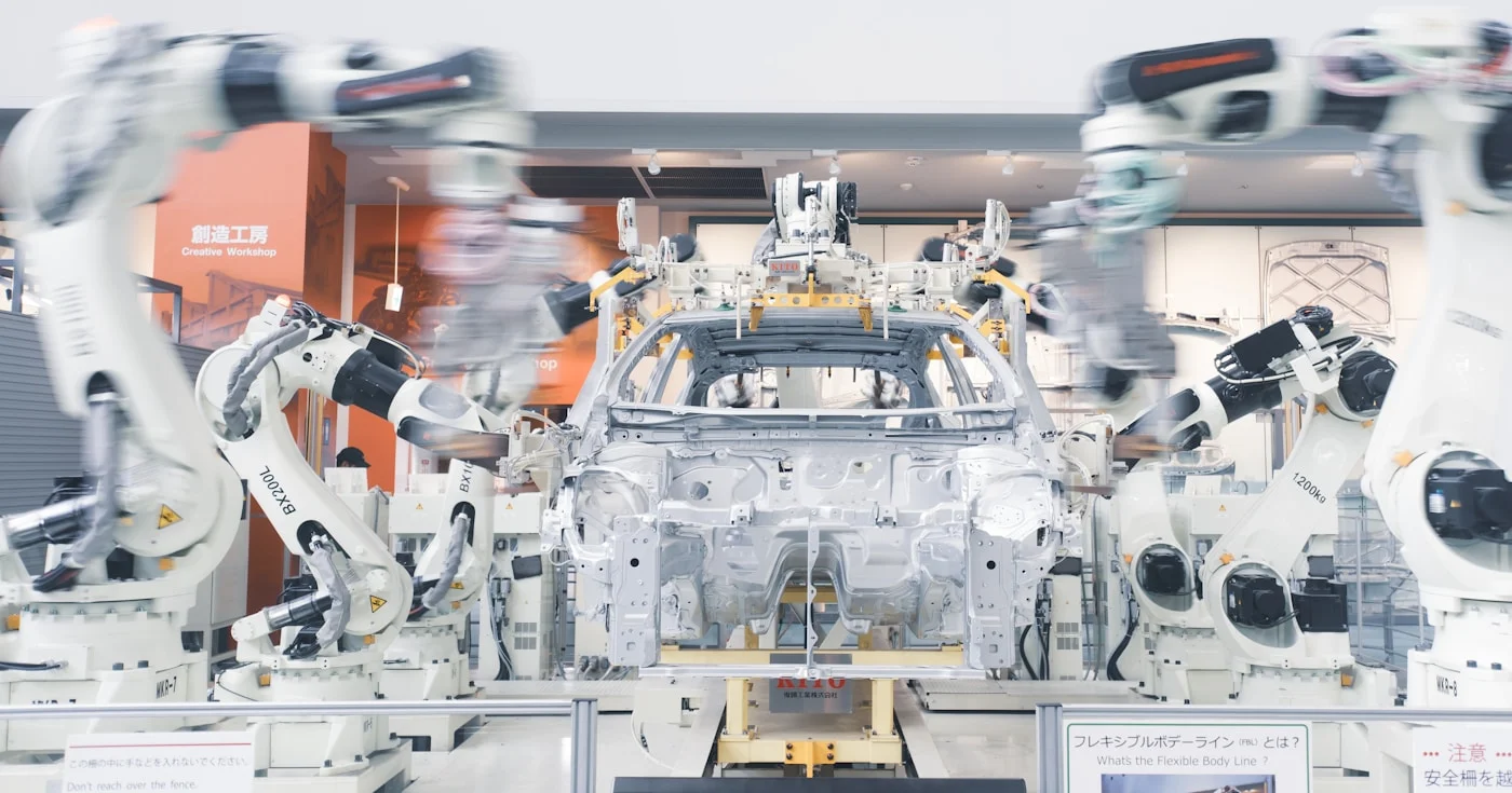 Robotic arms assembling a car chassis on a factory line, illustrating the Elon Musk Algorithm applied to manufacturing